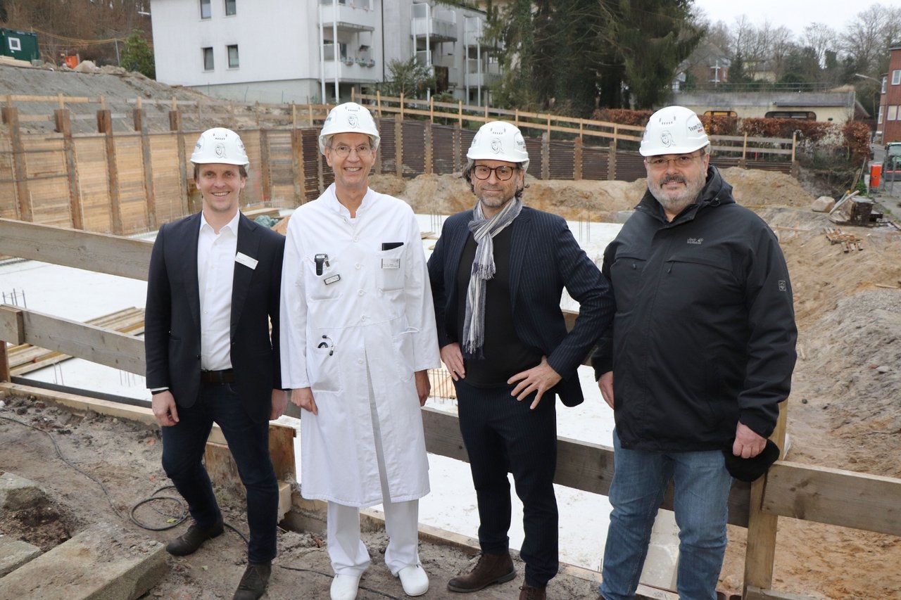 Vier Männer mit Schutzhelmen stehen auf einer Baustelle vor dem Rohbau eines Gebäudes auf dem Gelände des Krankenhauses Reinbek.