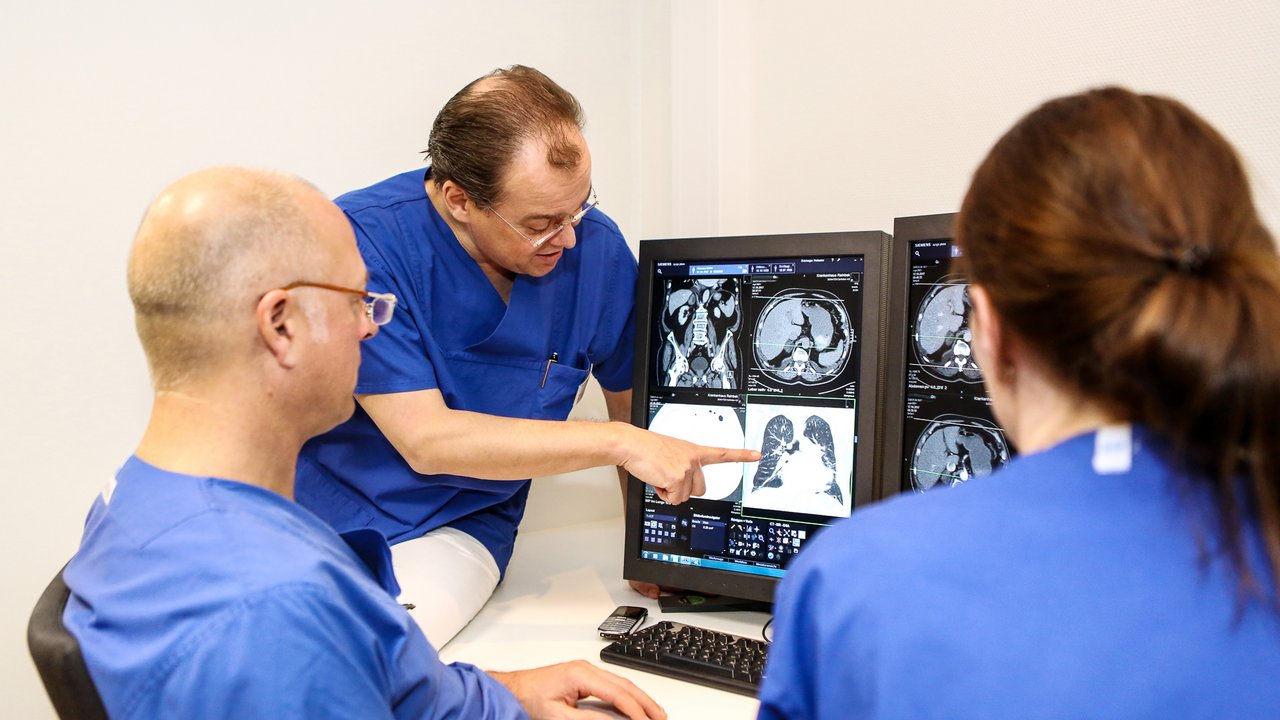 3 Radiologen schauen sich ein Bild auf dem Bildschirm an und diskutieren