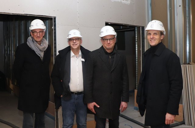 Vier Männer mit Schutzhelmen stehen auf einer Baustelle im Krankenhaus Reinbek in einem unfertigen Innenraum nebeneinander und blicken in die Kamera.