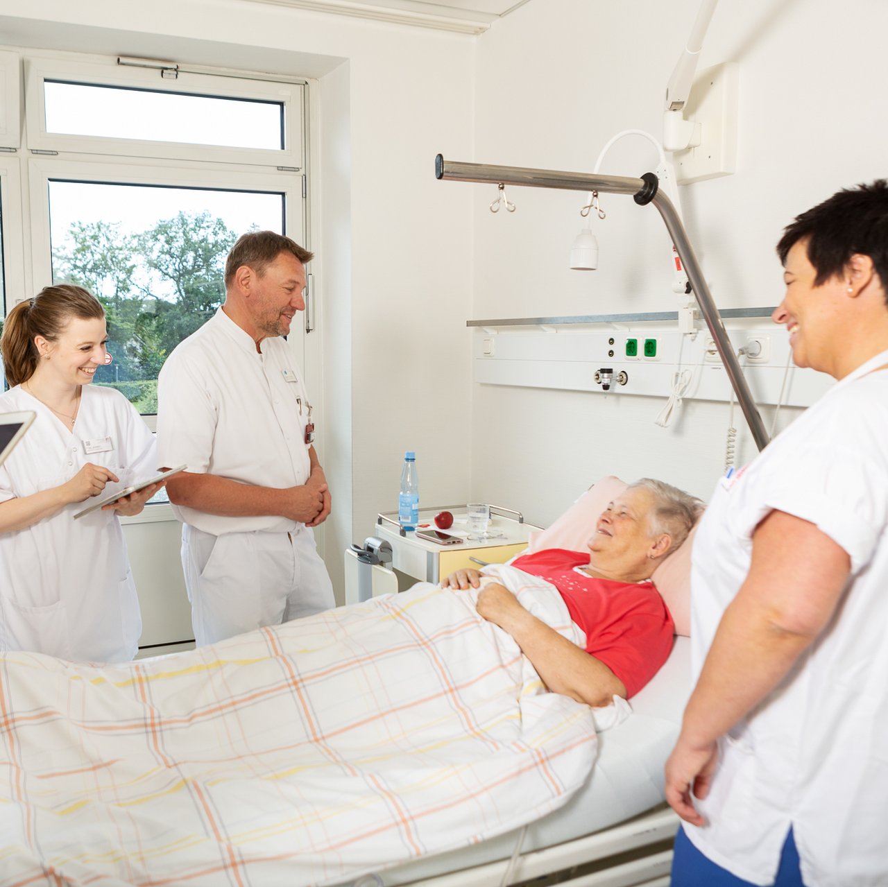 Ein Arzt und Pfleger:innen stehen um das Krankenhausbett einer Patientin bei einer Visite