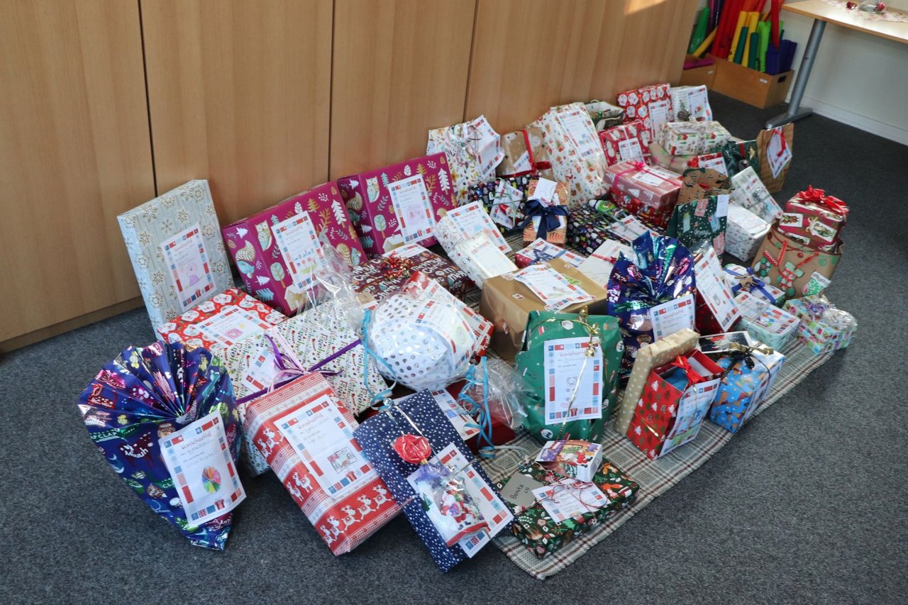 Viele verpackte Geschenke liegen auf einer Decke auf dem Boden in einem Raum.