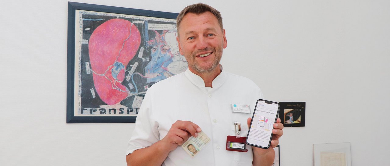 Ein Arzt hält seinen Personalausweis und Handy mit der Website für das Organspende Register in die Kamera