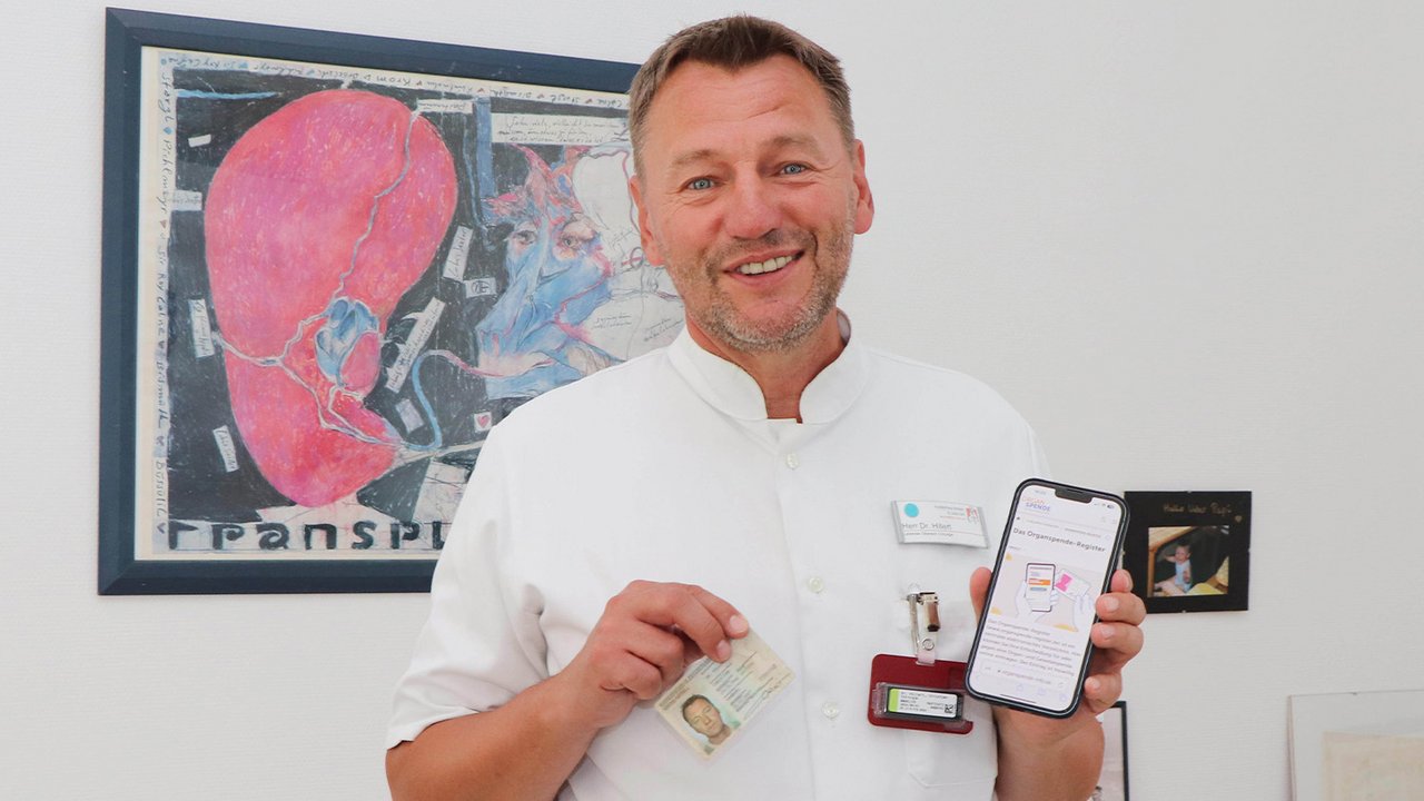 Ein Arzt hält seinen Personalausweis und Handy mit der Website für das Organspende Register in die Kamera