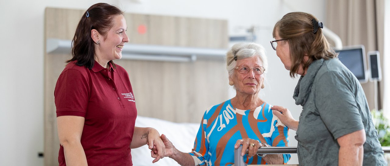 Eine Mitarbeiterin der Familiaren Pflege berät eine Patientin und ihre Tochter am Patientenbett