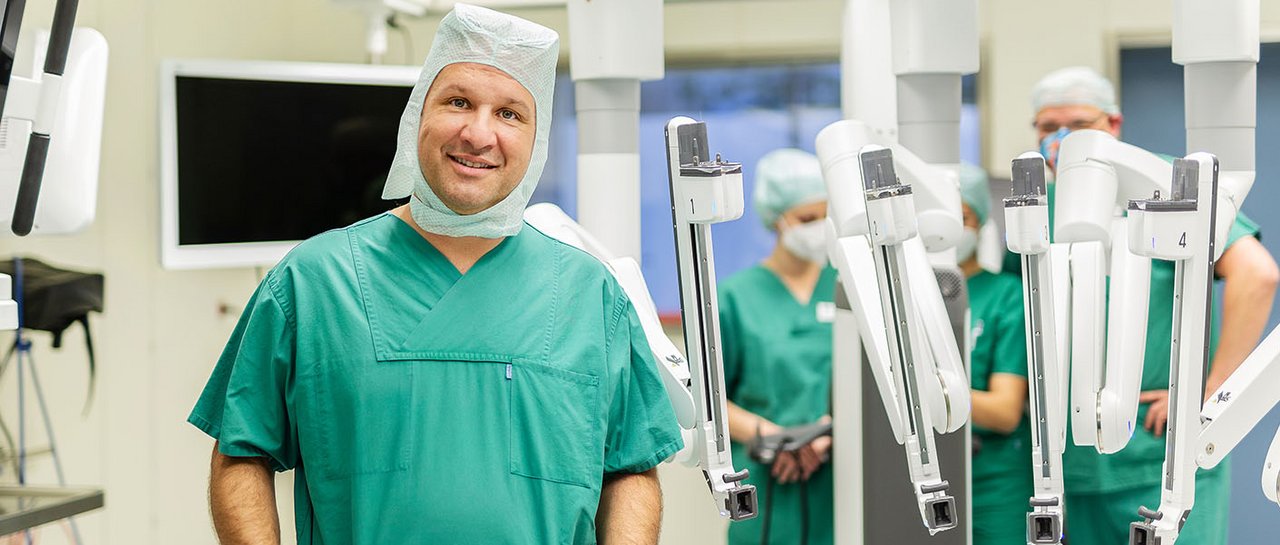 Ein Operateur stolz vor dem Da Vinci Roboter, im Hintergrund OTAs