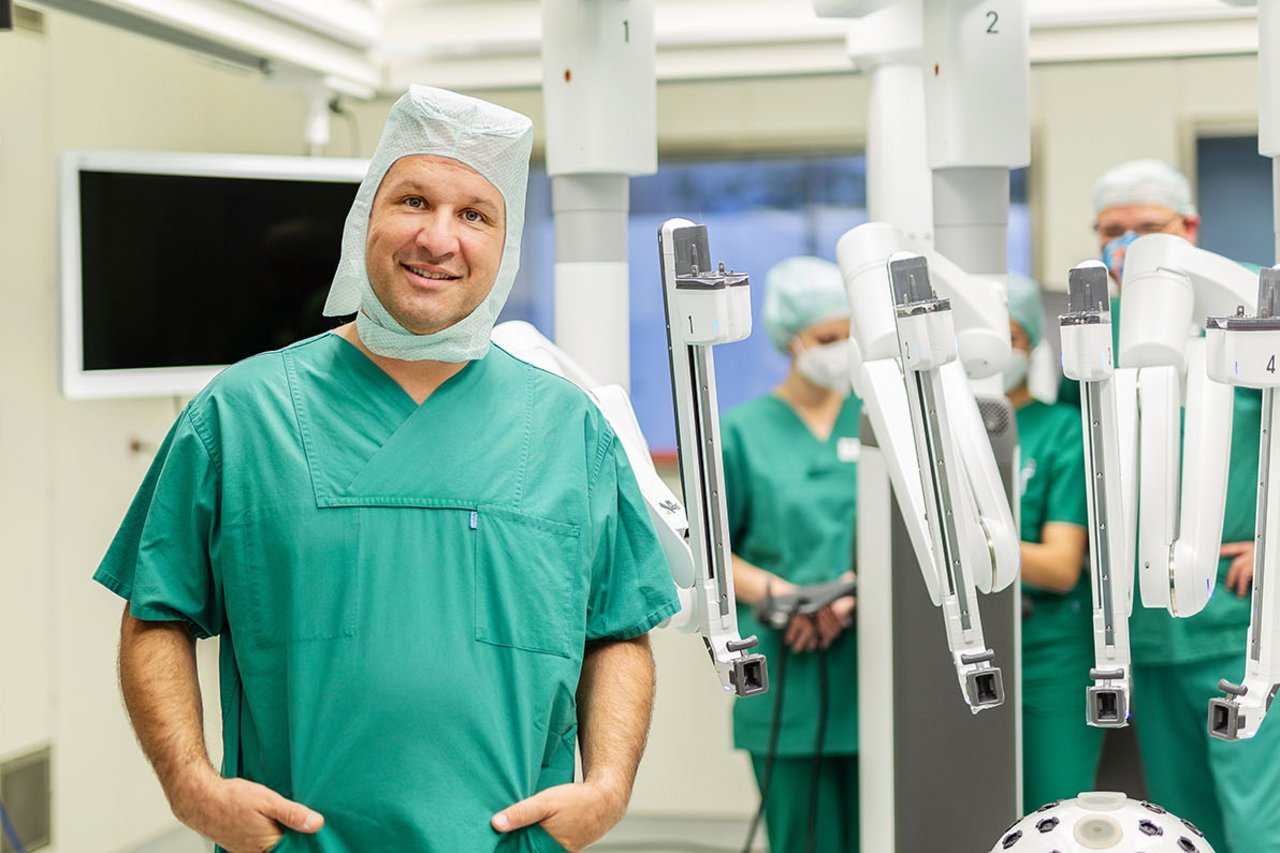 Ein Operateur stolz vor dem Da Vinci Roboter, im Hintergrund OTAs
