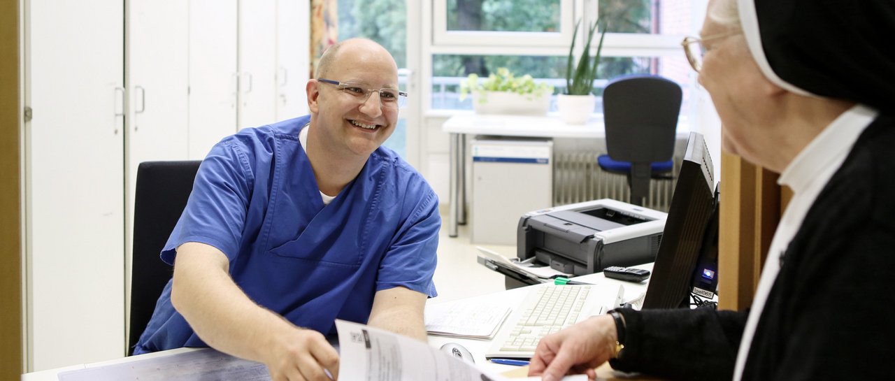 Ein Krankenhausmitarbeiter händigt ein Dokument an ein ältere Patientin aus.