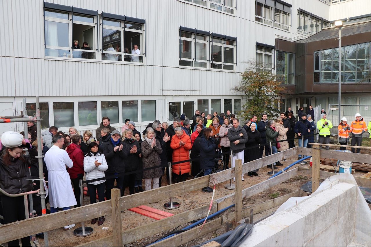 Gruppe von Mitarbeitenden und Gästen steht vor einer Baustelle am Krankenhaus Reinbek und beobachtet die Grundsteinlegung.