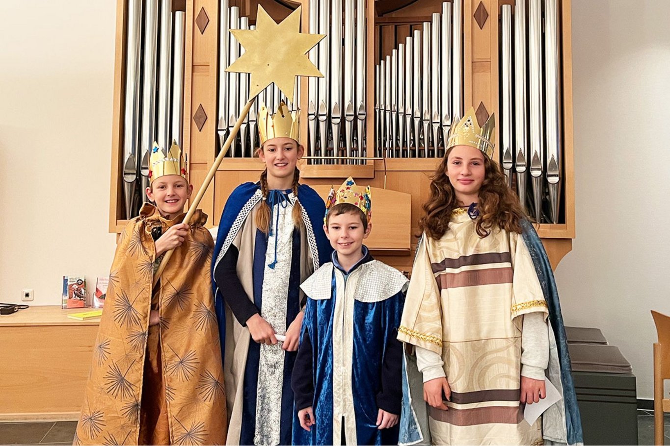 Vier als Sternsinger verkleidete Kinder mit Kronen und Umhängen stehen vor der Orgel in der Kapelle des Krankenhauses Reinbek; eines hält einen Stern auf einer Stange.