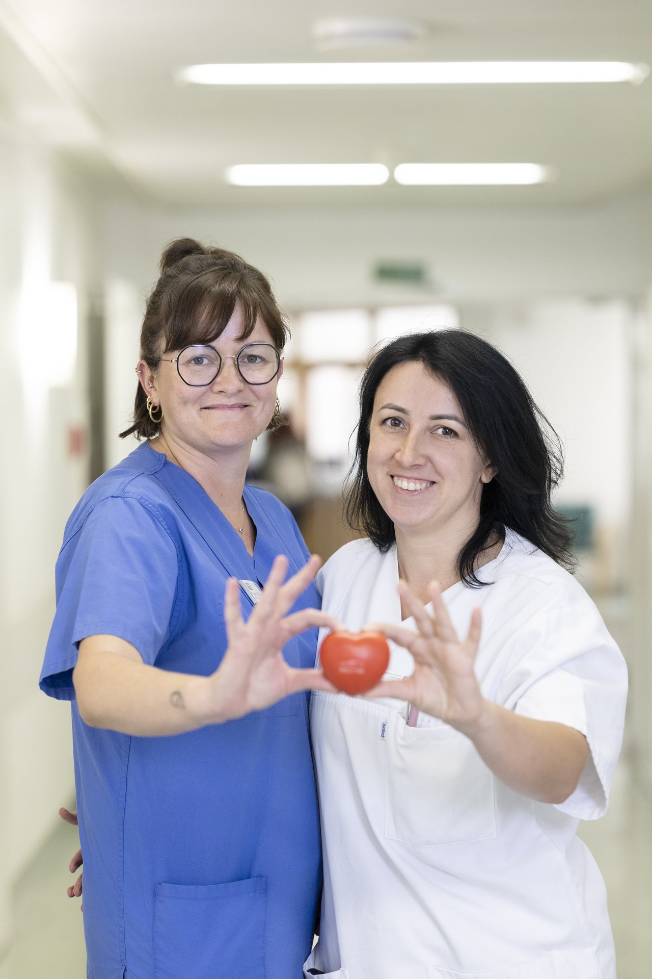 2 Mitarbeiterinnen der Kardiologie halten ein rotes Herz zusammen fest und lächeln in die Kamera