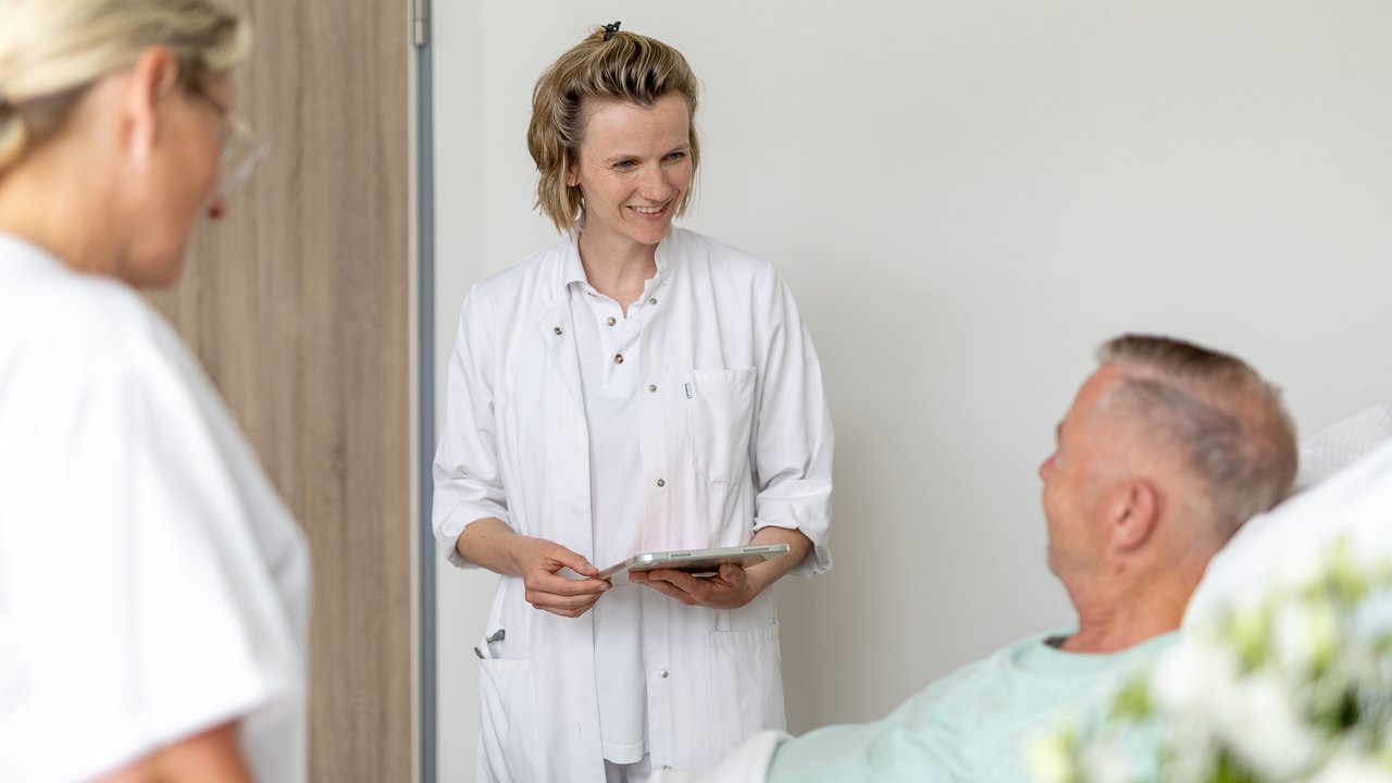 Eine junge Ärztin spricht mit einem Patienten, der im Krankenhausbett liegt