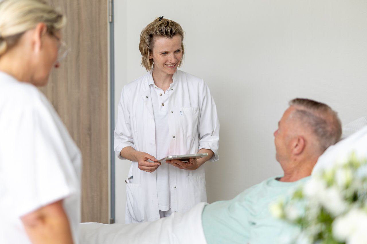 Eine junge Ärztin spricht mit einem Patienten, der im Krankenhausbett liegt