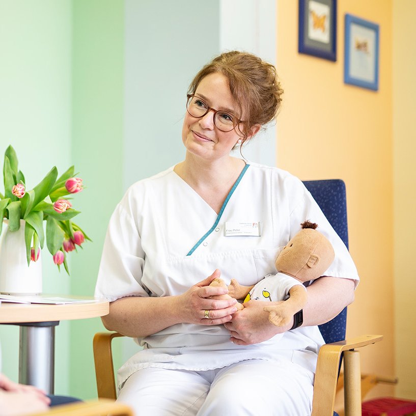 Eine Pflegerin sitzt mit einem Teddybär im Arm