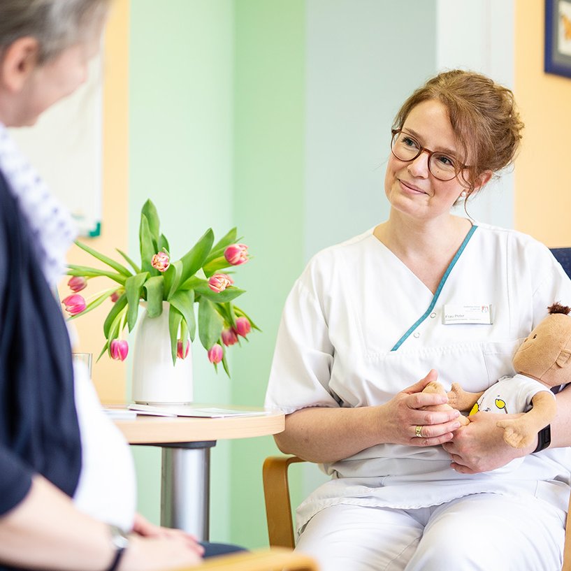 Eine Pflegerin sitzt mit einem Teddybär im Arm