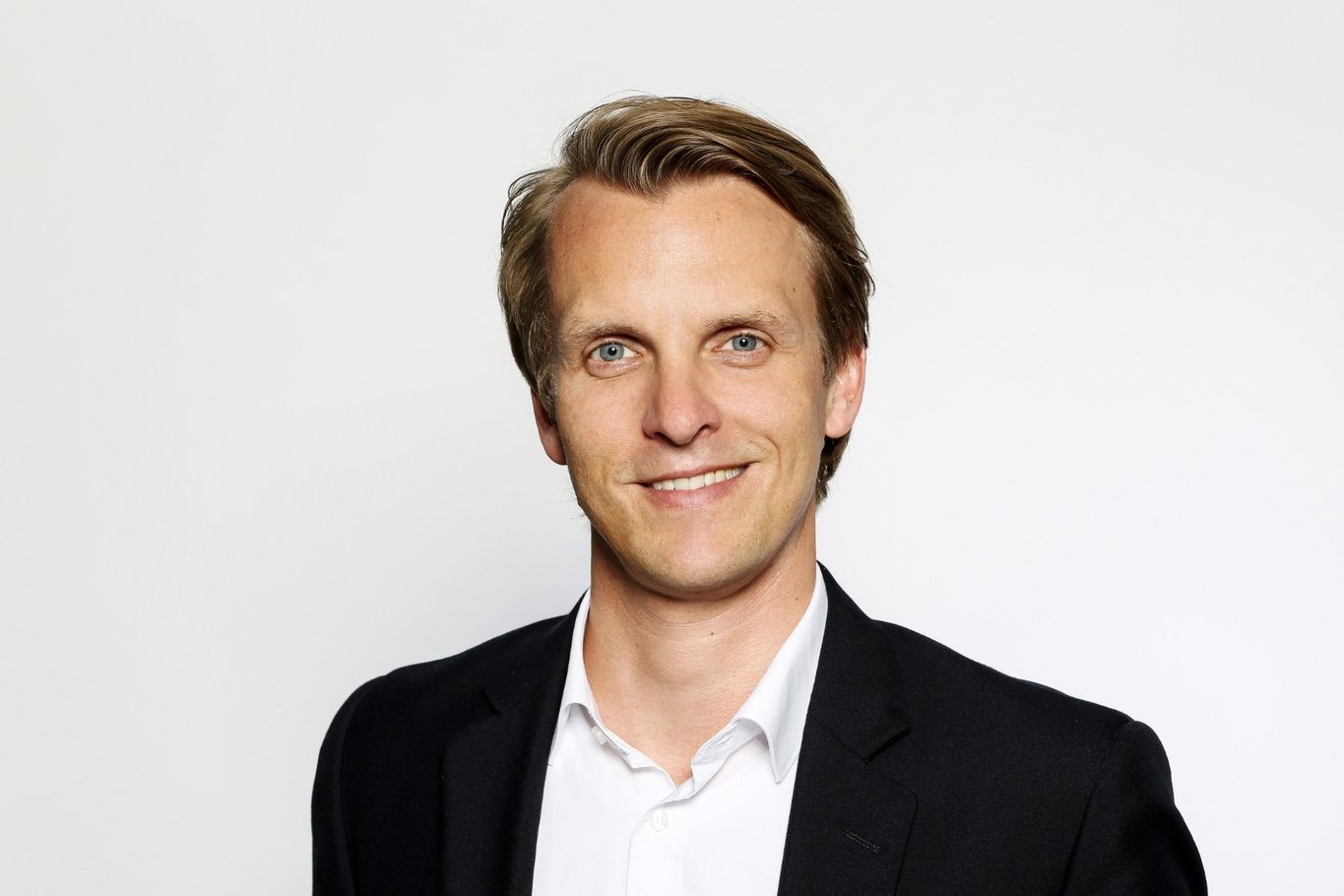 Porträt von Fabian Linke im schwarzen Sakko und weißen Hemd vor hellem Hintergrund.