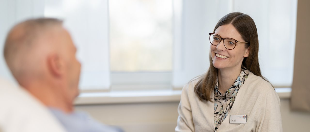 Eine Psychologin sitzt am Patientenbett und spricht mit einem Patienten