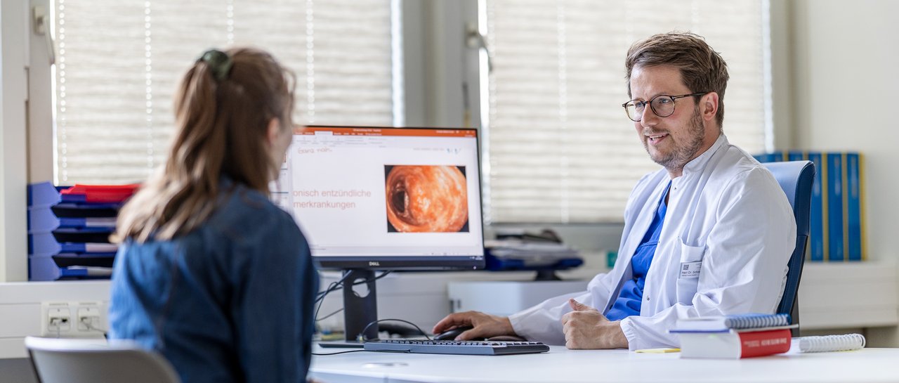 Eine Patientin spricht mit dem Arzt in einer Sprechstunde, während der Arzt etwas auf dem Computerbildschirm zeigt