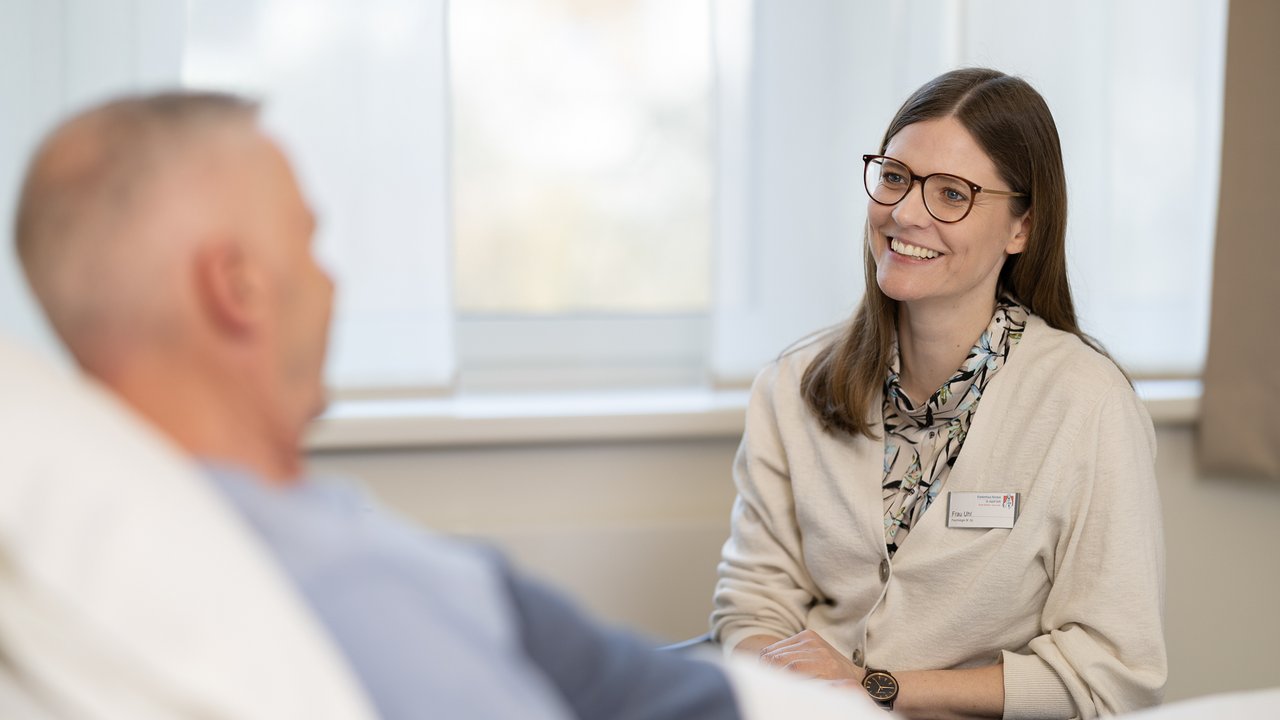 Eine Psychologin sitzt am Patientenbett und spricht mit einem Patienten