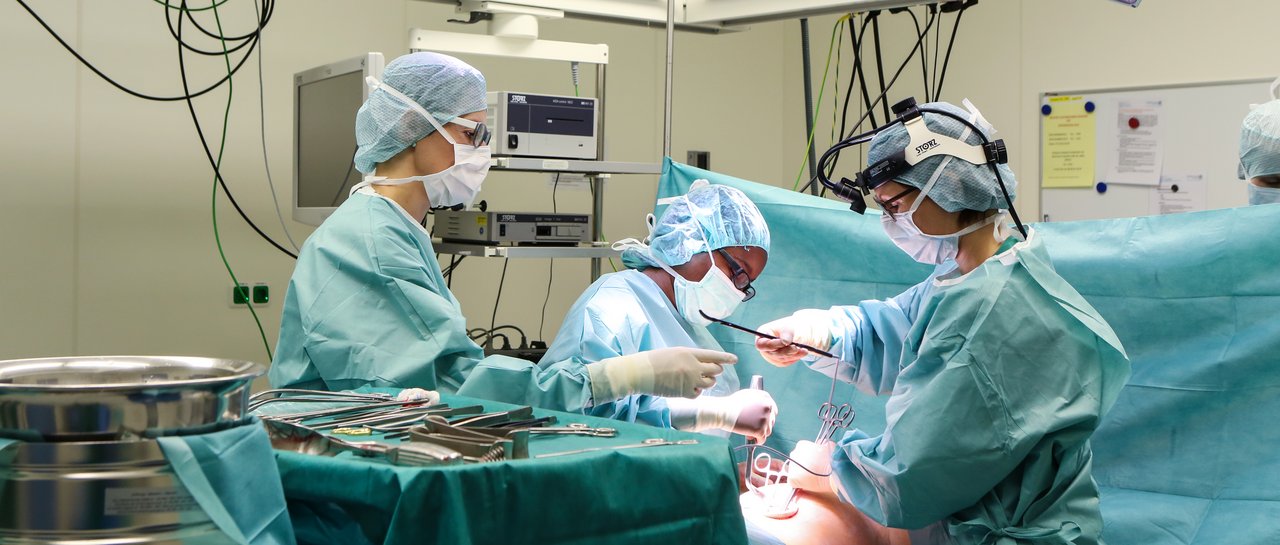 3 Personen, Ärztin und Assistenten stehen am OP-Tisch und operieren