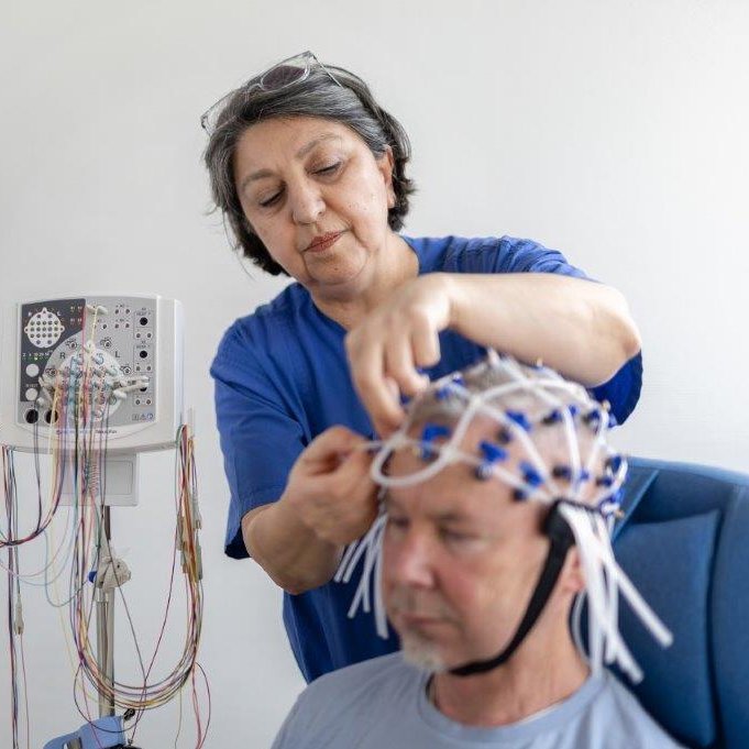 Einem Neurologiepatienten wird eine EEG-Haube aufgesetzt durch eine Pflegekraft