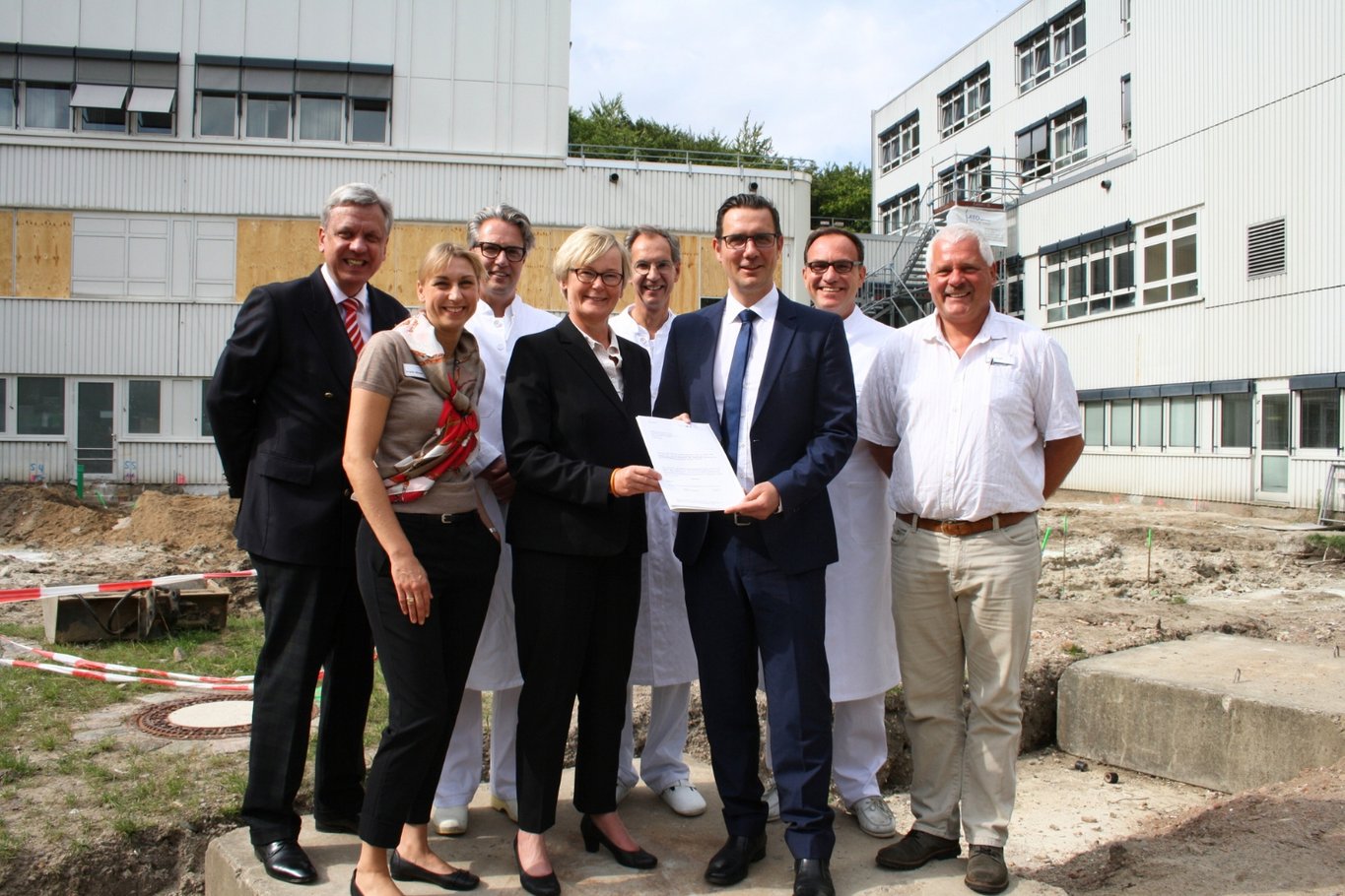 Mehrere Vertreter aus Politik und Krankenhaus stehen auf einer Baustelle am Krankenhaus Reinbek St. Adolf-Stift und präsentieren einen Förderbescheid für Bauprojekte.