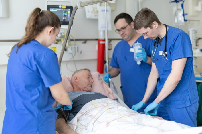 Ein Neurologiepatient wird von 3 Pflegekräften am Krankenhausbett versorgt