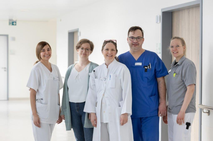 Das Team der Neurologie steht auf dem Krankenhausflur und lächelt in die Kamera