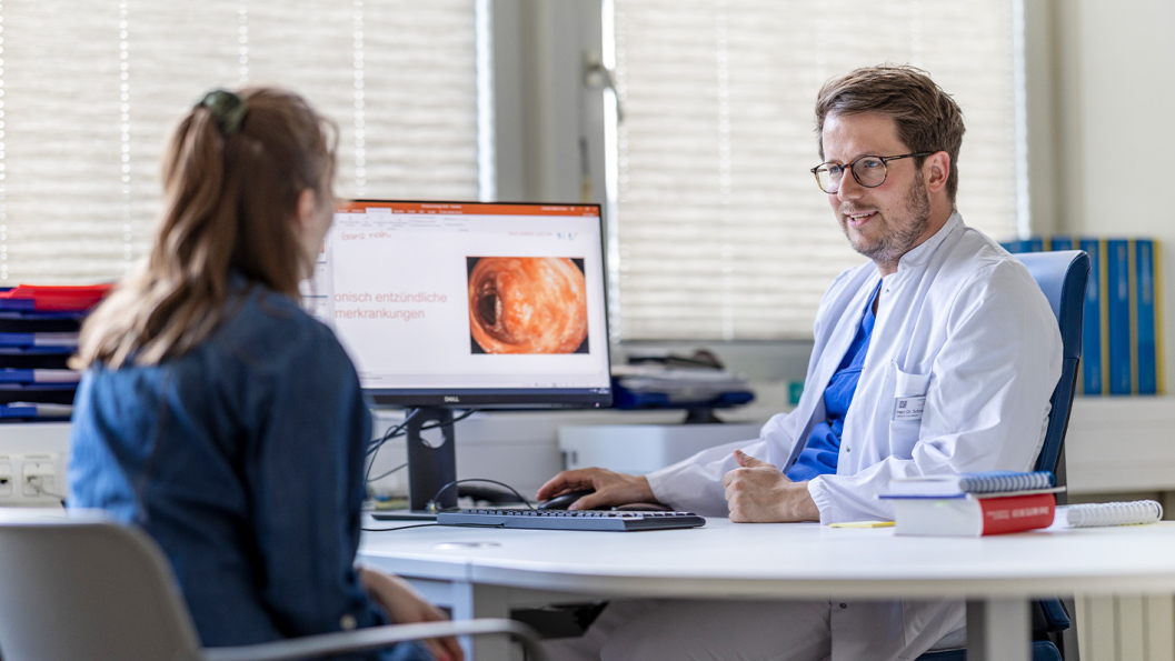 Dr. Schneider erklärt Patientin am Bildschirm auf dem Schreibtisch etwas zur chronisch entzündlichen Darmerkrankung