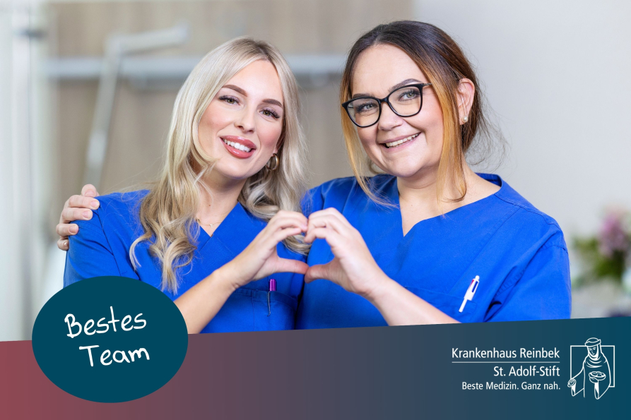 2 Pflegekräfte formen gemeinsam ein Herz mit ihren Händen und lächeln in die Kamera. Sie stehen in einem Patientenzimmer vor dem Krankenhausbett.