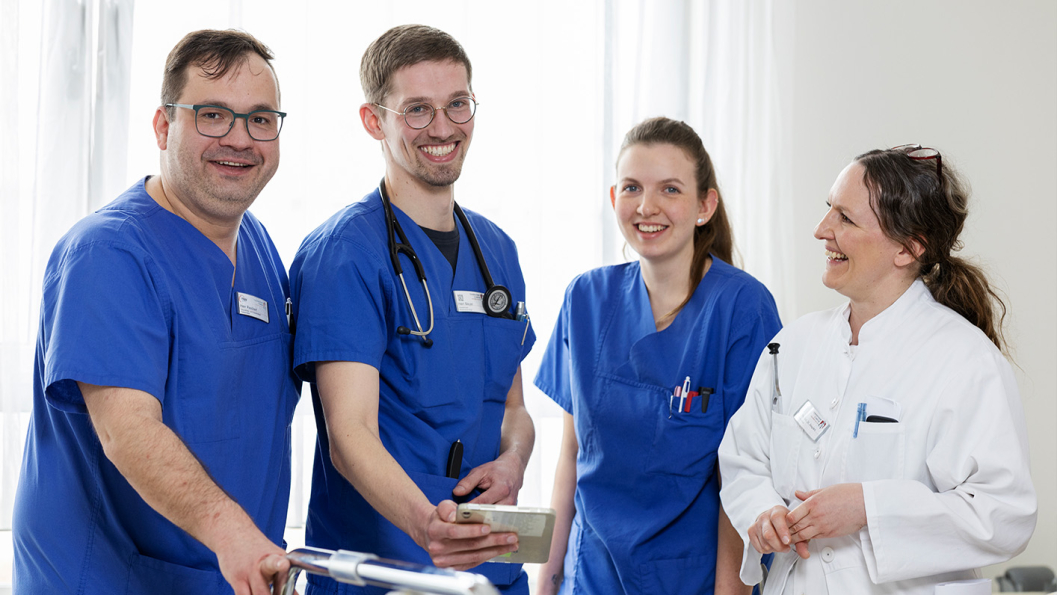 Das Team der Neurologie steht am Patientenbett und lächelt sich gegenseitig an.