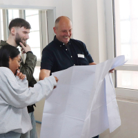 Der Technische Leiter schaut sich mit  zwei Azubis die Architektenpläne des neuen Campus für Gesundheitsberufe an
