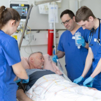 Ein Neurologiepatient wird von 3 Pflegekräften am Krankenhausbett versorgt