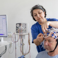 Einem Neurologiepatienten wird eine EEG-Haube aufgesetzt durch eine Pflegekraft