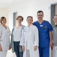 Das Team der Neurologie steht auf dem Krankenhausflur und lächelt in die Kamera