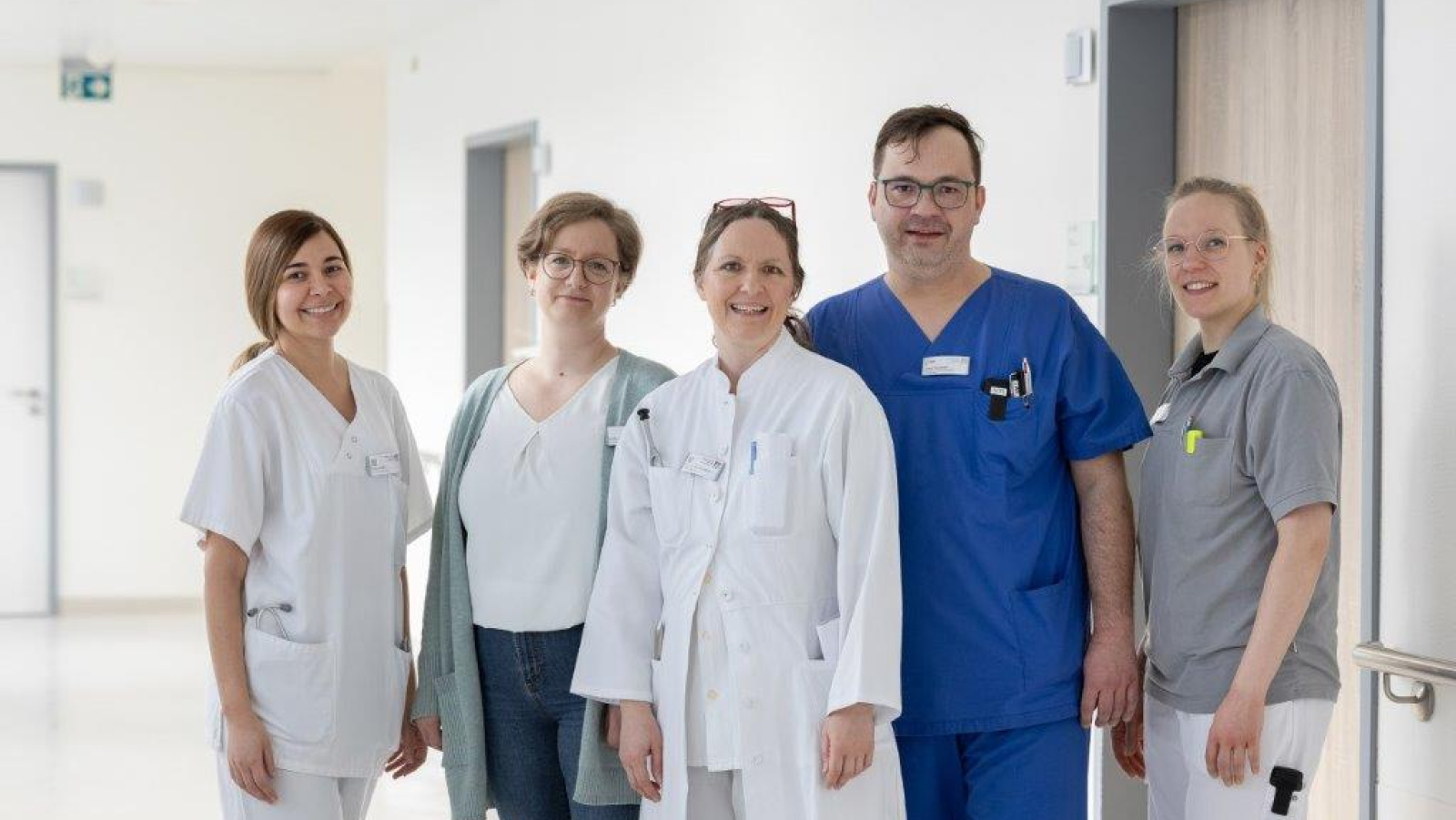 Das Team der Neurologie steht auf dem Krankenhausflur und lächelt in die Kamera