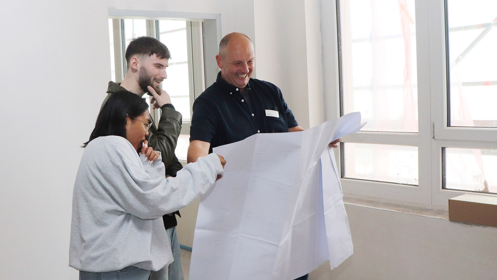 Der Technische Leiter schaut sich mit  zwei Azubis die Architektenpläne des neuen Campus für Gesundheitsberufe an