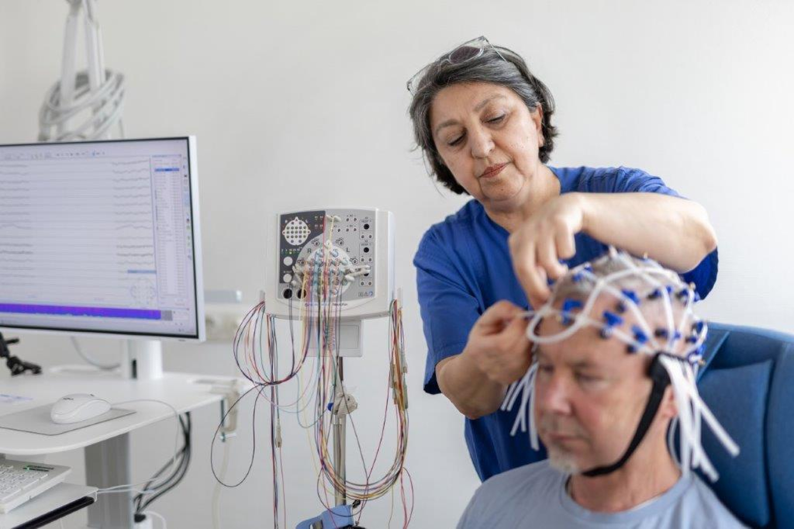 Einem Neurologiepatienten wird eine EEG-Haube aufgesetzt durch eine Pflegekraft