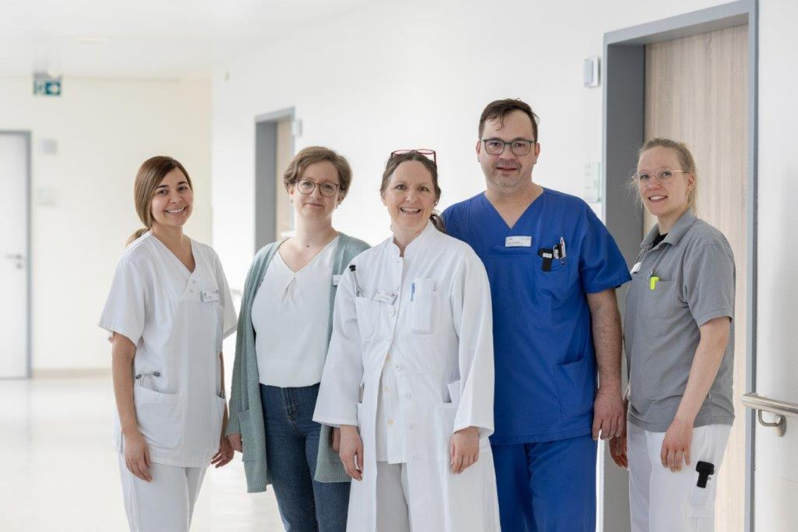 Das Team der Neurologie steht auf dem Krankenhausflur und lächelt in die Kamera
