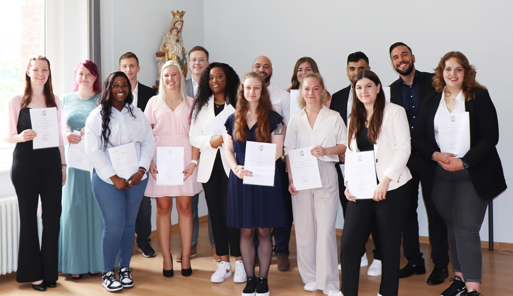 Stolz halten 15 generalistisch ausgebildete Pflegefachkräfte ihre Examensurkunden in der Hand