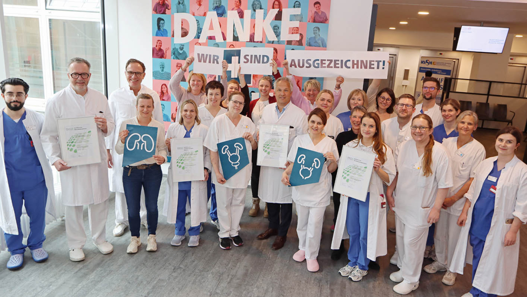 Viele Mitarbeitende aus verschiedenen Krankenhaus-Berufsgruppen halten Zertifikate hoch