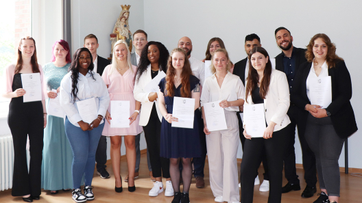 Stolz halten 15 generalistisch ausgebildete Pflegefachkräfte ihre Examensurkunden in der Hand