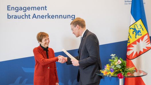 Daniel Günther verleiht eine Ehrennadel an eine Grüne Dame