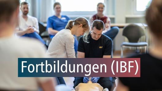 In einer Fortbildung wir eine Reanimationsübung an einer Puppe gezeigt. Darum ein Stuhlkreis an Teilnehmenden. Unten steht ein Text: "Fortbildungen (IBF)"