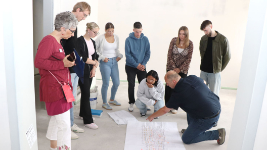 Auszubildende beugen sich über einen Bauplan auf der Baustelle ihrer neuen Schule