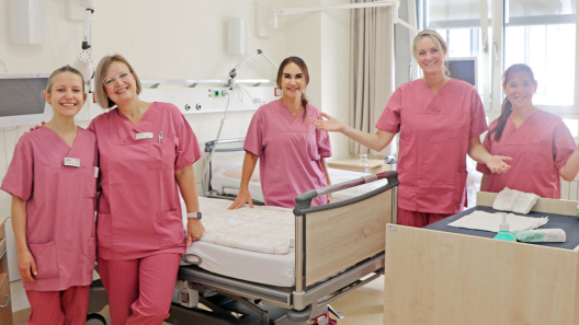 3 Hebammen und 2 Krankenschwestern in einem Patientenzimmer